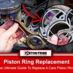 A close-up of a person's hand holding two broken piston rings in front of an engine block, which has a partially disassembled piston visible inside one of the cylinders. The engine appears to be in the process of repair, with oil and grime visible on the components.