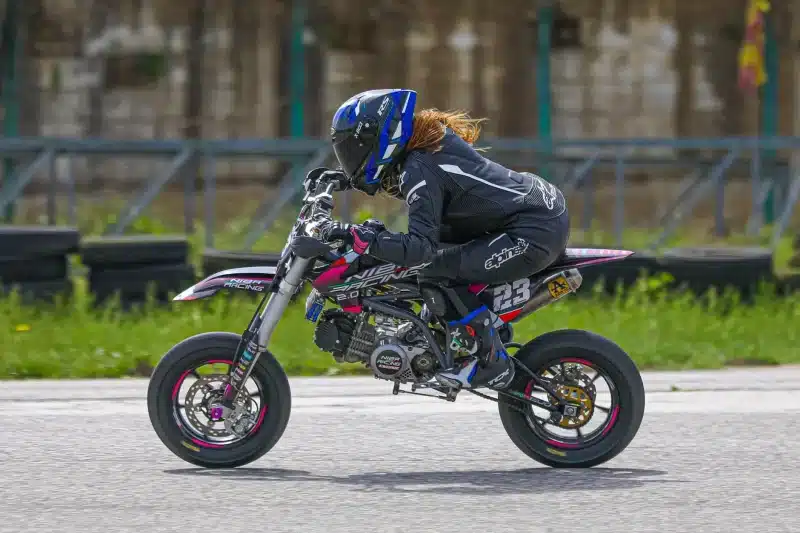 A woman wearing safety gear races on a mini dirt bike outdoors, showcasing speed and control.