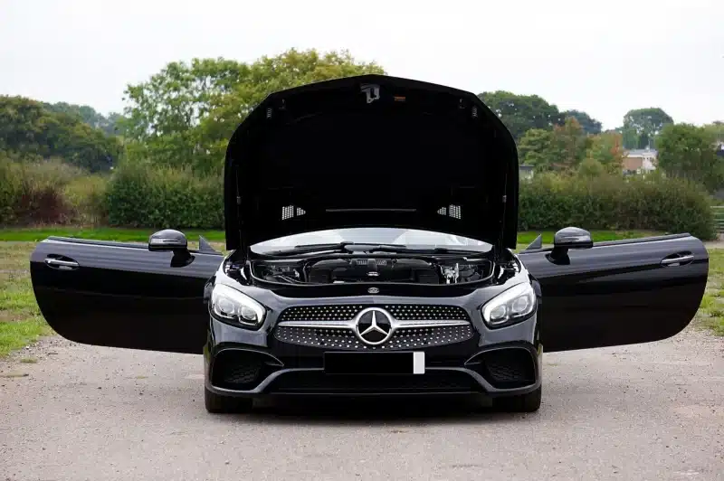 Front view of a black Mercedes-Benz AMG with opened doors and hood, showcasing its engine.