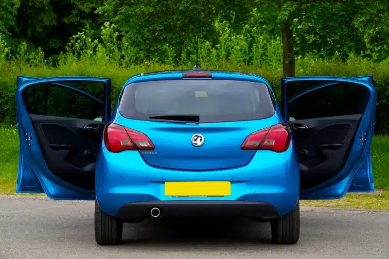 Rear view of a blue Vauxhall Corsa with open doors on a street.