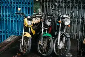 Three parked motorcycles in urban area, vibrant colors and metal grate backdrop.