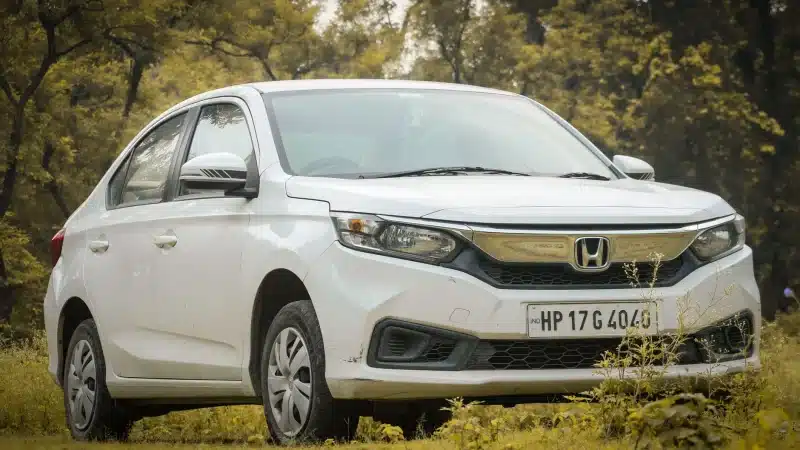 White sedan car parked outdoors with scenic foliage background.