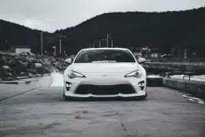 White sports car parked on a coastal road with an overcast sky background, exuding a cool and dramatic vibe.
