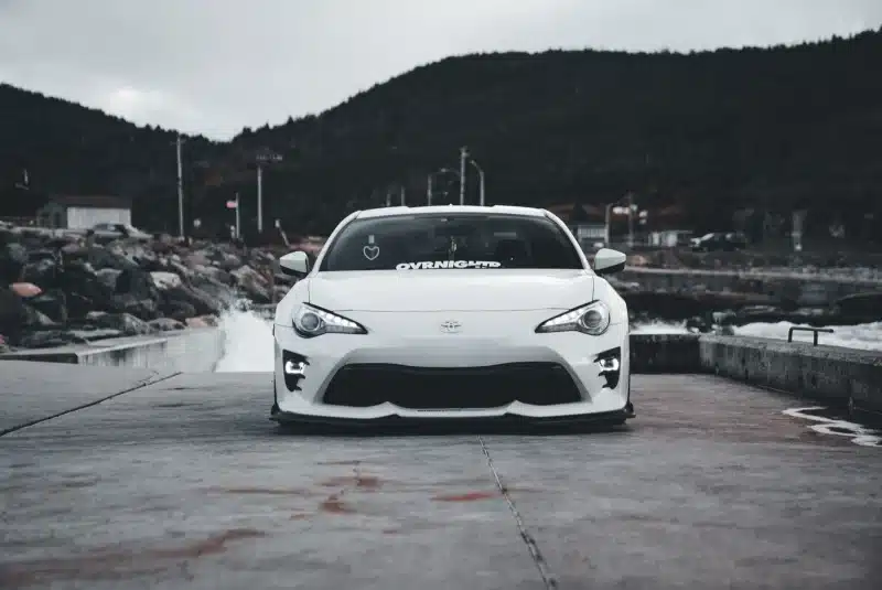 White sports car parked on a coastal road with an overcast sky background, exuding a cool and dramatic vibe.