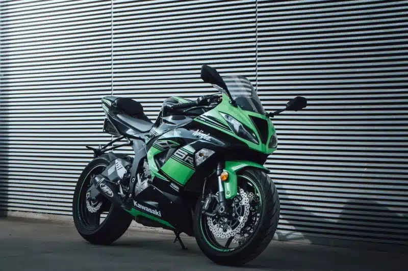 A vibrant green Kawasaki Ninja motorcycle parked outdoors against a modern corrugated metal wall.