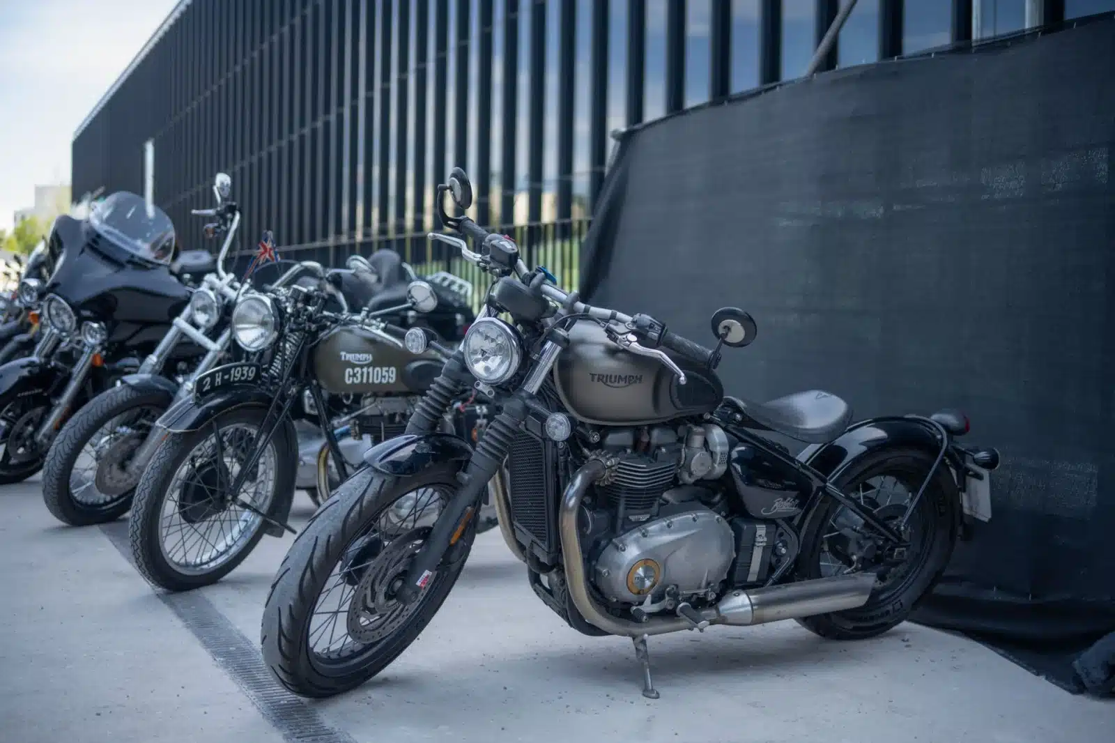 Lineup of Triumph motorcycles parked outdoors with modern architecture backdrop.