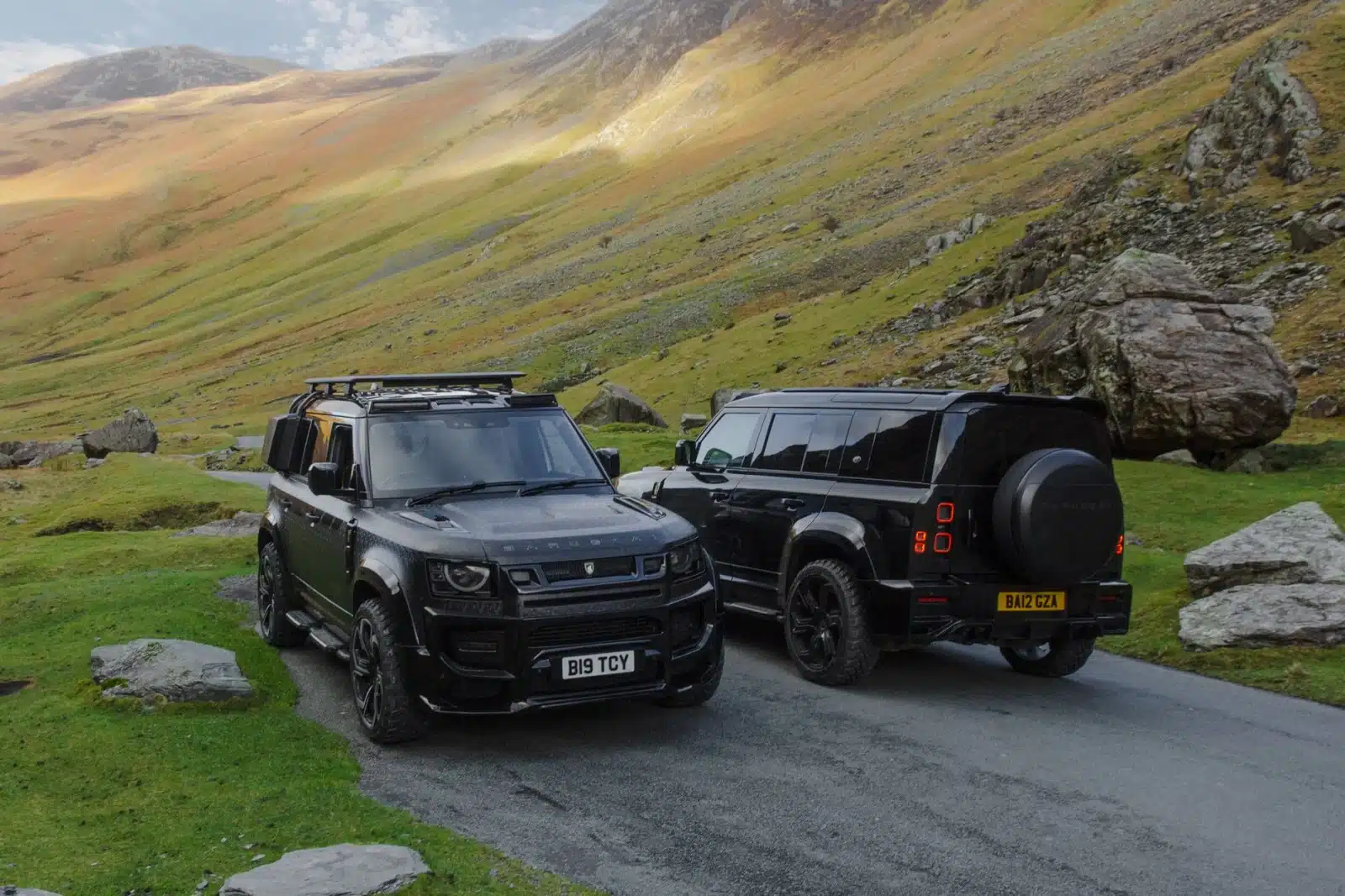 Two black Land Rover Defenders parked in a picturesque valley, showcasing rugged terrain.