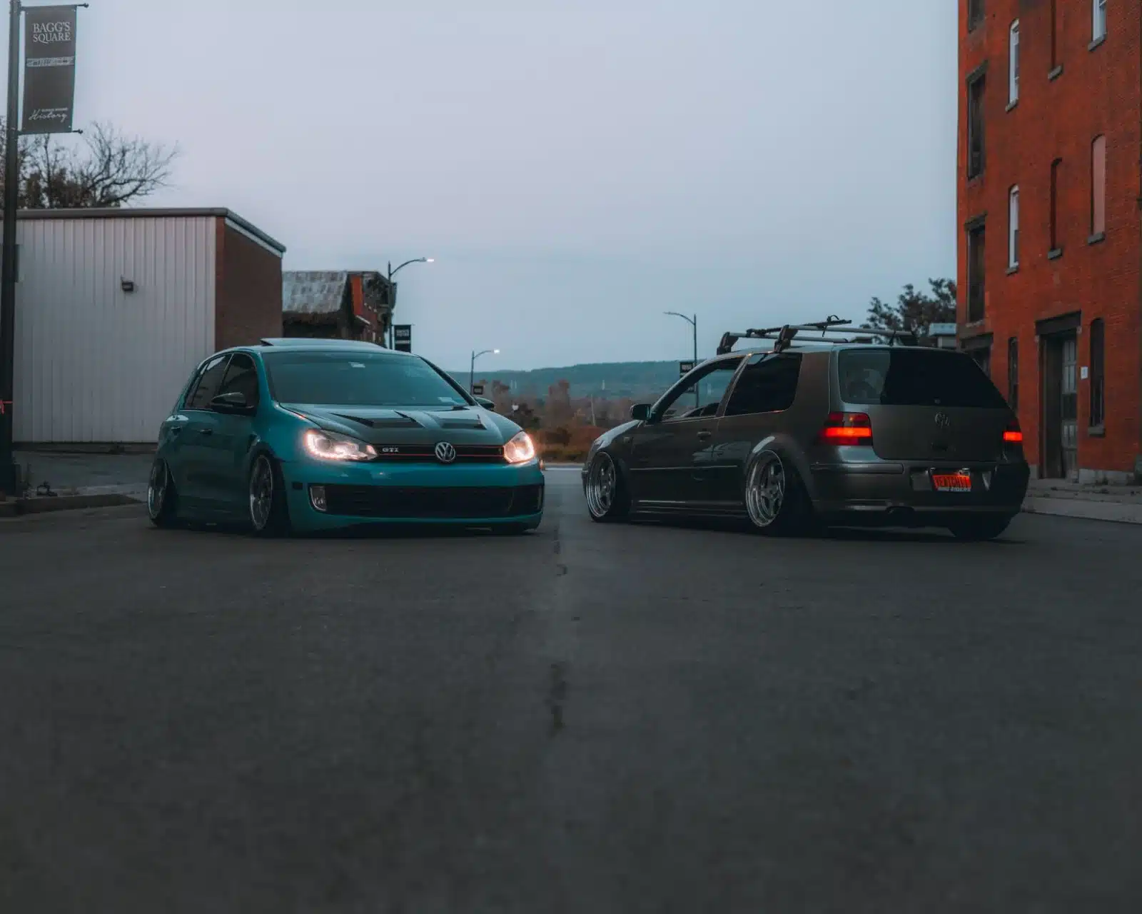 Two Volkswagen cars parked on a city street during twilight, showcasing urban automotive lifestyle.