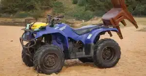 A blue quad bike with chairs on a sandy beach near greenery.
