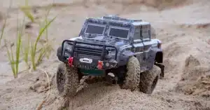 Close-up of a toy RC car navigating through a sandy off-road terrain, showcasing its rugged design.